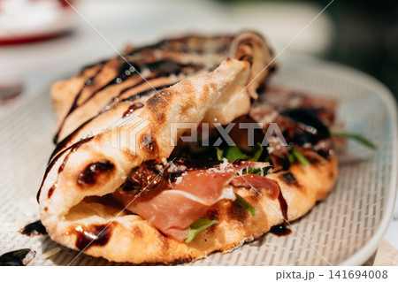 Crispy folded flatbread filled with prosciutto, greens and cheese, finished with balsamic glaze. Gourmet street food presentation creates a premium lunch concept Crispy folded flatbread filled with prosciutto, greens and cheese, finished with balsamic glaze. Gourmet street food presentation creates a premium lunch concept 141694008
