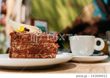 Rich chocolate layer cake served with fresh coffee in a cozy cafe setting. Indulgent dessert and premium coffee create a warm lifestyle treat concept Rich chocolate layer cake served with fresh coffee in a cozy cafe setting. Indulgent dessert and premium coffee create a warm lifestyle treat concept 141694012