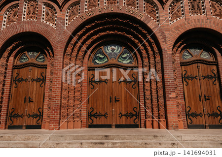 Ornate wooden entrance doors of Subotica Synagogue in Subotica, Serbia. Decorative brick arches and carved details highlight historic craftsmanship Ornate wooden entrance doors of Subotica Synagogue in Subotica, Serbia. Decorative brick arches and carved details highlight historic craftsmanship 141694031