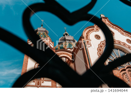Subotica Synagogue seen through decorative iron fence in Subotica, Serbia. Artistic view of historic Art Nouveau landmark with ornate details 141694044