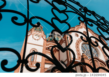 Subotica Synagogue seen through decorative iron fence in Subotica, Serbia. Artistic view of historic Art Nouveau landmark with ornate details 141694045