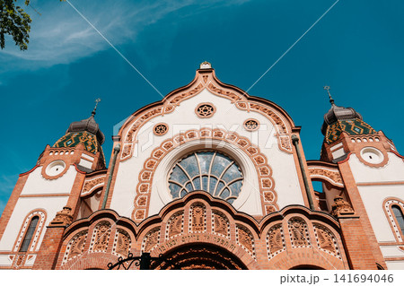 Decorative facade of Subotica Synagogue under vivid blue sky in Subotica, Serbia. Art Nouveau architecture with ornate brickwork and ceramic roof details Decorative facade of Subotica Synagogue under vivid blue sky in Subotica, Serbia. Art Nouveau architecture with ornate brickwork and ceramic roof details 141694046
