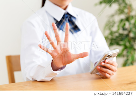 リビングのテーブルでスマホを見て指を5本立てる制服姿の中学生 リビングのテーブルでスマホを見て指を5本立てる制服姿の中学生 141694227