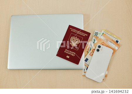 Russian passport lies on euro banknotes beside a laptop and smartphone on a desk. Concept of relocation from Russia, remote work setup and financial planning for moving abroad Russian passport lies on euro banknotes beside a laptop and smartphone on a desk. Concept of relocation from Russia, remote work setup and financial planning for moving abroad 141694232