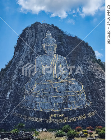 Golden outline Buddha image carved on cliff face with Thai flags at summit in Khao Chee Chan Pattaya Thailand Golden outline Buddha image carved on cliff face with Thai flags at summit in Khao Chee Chan Pattaya Thailand 141694425