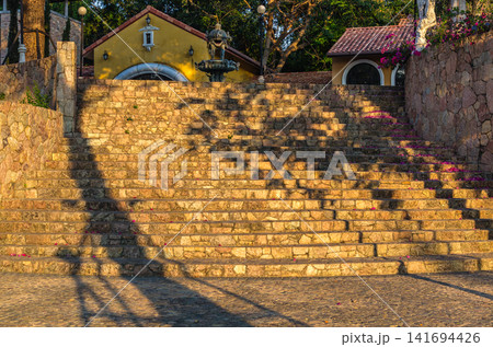 Wide stone staircase with tree shadows and decorative fountain on a Mediterranean-style building exterior in evening light 141694426