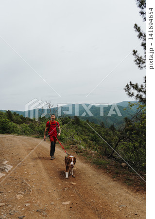 Man walking with Australian Shepherd on a mountain dirt road in Serbia. Concept of hiking, friendship, travel and healthy outdoor lifestyle 141694654