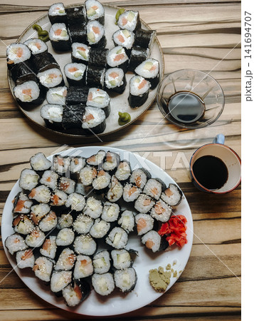Homemade sushi rolls served on plates with soy sauce, wasabi and pickled ginger on wooden table. Traditional japanese food arrangement with fresh ingredients Homemade sushi rolls served on plates with soy sauce, wasabi and pickled ginger on wooden table. Traditional japanese food arrangement with fresh ingredients 141694707