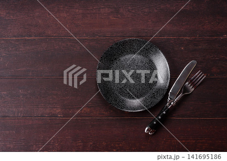 An empty round ceramic plate on a dark, textured brown background. An empty round plate An empty round ceramic plate on a dark, textured brown background. An empty round plate 141695186