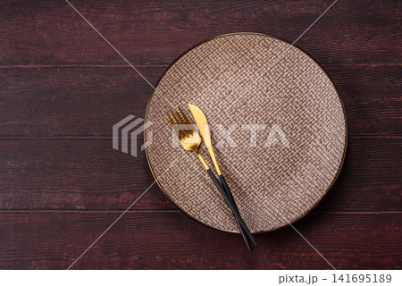 An empty round ceramic plate on a dark, textured brown background. An empty round plate 141695189