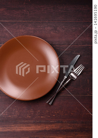 An empty round ceramic plate on a dark, textured brown background. An empty round plate An empty round ceramic plate on a dark, textured brown background. An empty round plate 141695190