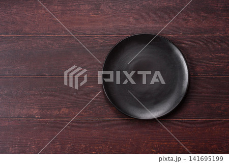 An empty round ceramic plate on a dark, textured brown background. An empty round plate An empty round ceramic plate on a dark, textured brown background. An empty round plate 141695199