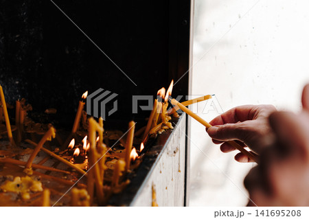 Human hand places thin candles into a religious prayer stand. Concept of faith, spirituality, remembrance and personal devotion Human hand places thin candles into a religious prayer stand. Concept of faith, spirituality, remembrance and personal devotion 141695208