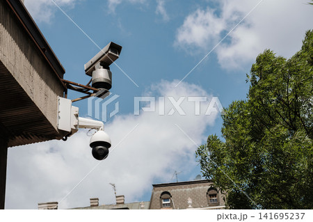 Security cameras mounted on a city building against blue cloudy sky in Belgrade Serbia. Concept of surveillance, monitoring, technology and public safety Security cameras mounted on a city building against blue cloudy sky in Belgrade Serbia. Concept of surveillance, monitoring, technology and public safety 141695237