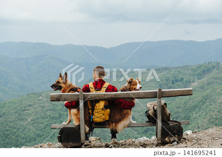 Male traveler sitting on a wooden bench with German Shepherd and Australian Shepherd in Serbian mountains. Concept of friendship, hiking and peaceful travel Male traveler sitting on a wooden bench with German Shepherd and Australian Shepherd in Serbian mountains. Concept of friendship, hiking and peaceful travel 141695241