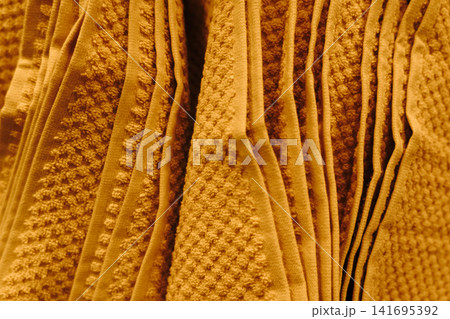 Beige textured towels hanging in rows under warm indoor lighting. Cozy bathroom textile and home furnishing concept 141695392