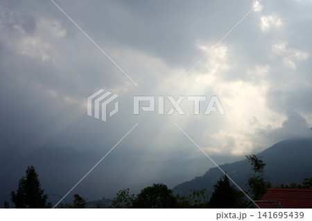 Dramatic sun rays piercing through dark storm clouds over mountain landscape 141695439