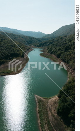 Aerial view of Zavoj Lake in Stara Planina National Park, Serbia, with turquoise water reflecting sunlight between green forested hills Aerial view of Zavoj Lake in Stara Planina National Park, Serbia, with turquoise water reflecting sunlight between green forested hills 141696033
