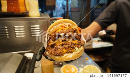 Large double patty burger with sauces held in gloved hand, fast food burger concept Large double patty burger with sauces held in gloved hand, fast food burger concept 141697177