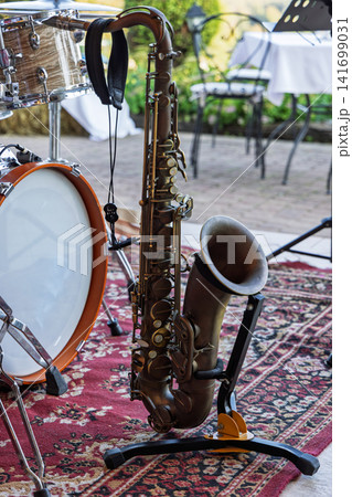 Tenor saxophone on a stand beside an acoustic drum kit on a garden patio 141699031