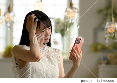 スマートフォンを見て悩む女性 141700000