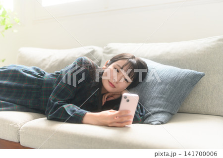 ソファでくつろぎながらスマホを見る女性 ソファでくつろぎながらスマホを見る女性 141700006