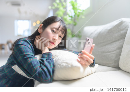 ソファでスマートフォンを操作する女性 ソファでスマートフォンを操作する女性 141700012