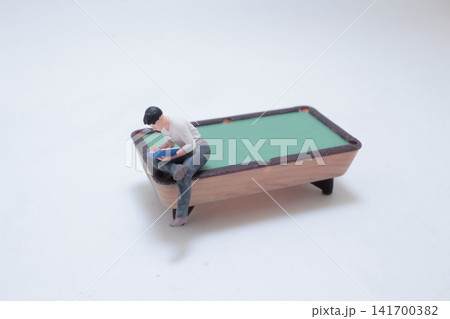Miniature man reading on pool table Miniature man reading on pool table 141700382