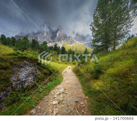 Hiking dirt path leading to mountain peaks in low clouds 141700668
