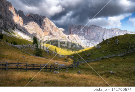 Wooden fence on green meadow with dirt road and mountain peaks Wooden fence on green meadow with dirt road and mountain peaks 141700674