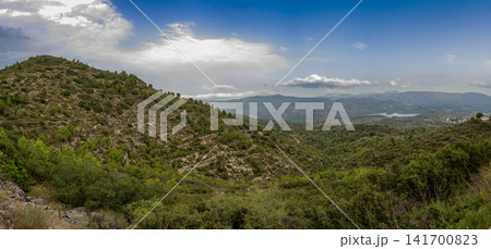 Panoramic view from Port de Beniarres pass showing hills, valley town, and reservoir under clouded blue sky Panoramic view from Port de Beniarres pass showing hills, valley town, and reservoir under clouded blue sky 141700823