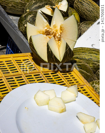 Sliced Piel de Sapo melon displayed on a market crate with fresh fruit slices on a white plate Sliced Piel de Sapo melon displayed on a market crate with fresh fruit slices on a white plate 141700831