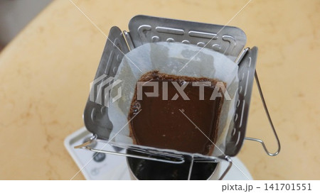Close-up of freshly ground coffee blooming in a white paper filter inside a stainless steel pour-over dripper. Dark, rich coffee grounds are saturated with hot water, creating a bubbling surface durin 141701551