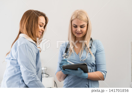 Confident female physician discussing health information with a patient while using a tablet in a bright clinic. Modern healthcare technology and patient care interaction in a clinical setting Confident female physician discussing health information with a patient while using a tablet in a bright clinic. Modern healthcare technology and patient care interaction in a clinical setting 141701856
