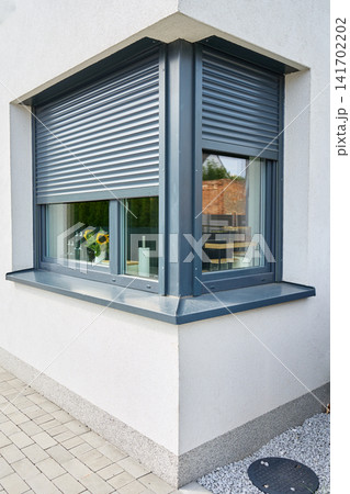 Partially lowered roller shutters cover two corner windows on a modern house, with kitchen items visible inside Partially lowered roller shutters cover two corner windows on a modern house, with kitchen items visible inside 141702202