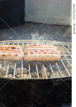 バーべーキューコンロの上に並べられたソーセージ 自宅でのバーベキュー・ディナー バーべーキューコンロの上に並べられたソーセージ 自宅でのバーベキュー・ディナー 141702384