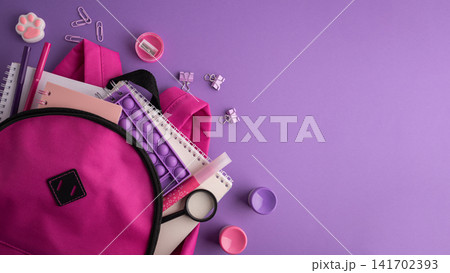Pink backpack overflowing with colorful school supplies and stationery on a vibrant purple background Pink backpack overflowing with colorful school supplies and stationery on a vibrant purple background 141702393