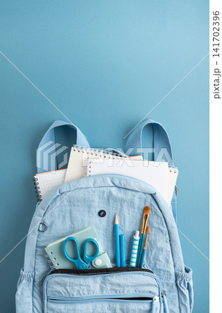 Light blue backpack with notebooks pencils scissors and brushes on a blue background Light blue backpack with notebooks pencils scissors and brushes on a blue background 141702396