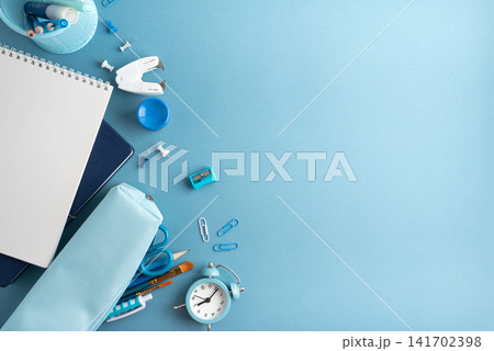 A flat lay of school and art supplies on a blue background with a notebook pencil case and alarm clock A flat lay of school and art supplies on a blue background with a notebook pencil case and alarm clock 141702398