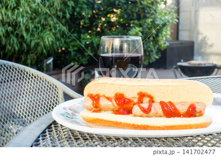 バーベキューで焼けたソーセージのホットドックとグラスの赤ワイン　庭で楽しむバーベキュー・ディナー 141702477