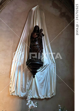 Wooden Statue of Madonna and Child in Church Niche with White Satin Drapery. Wooden Statue of Madonna and Child in Church Niche with White Satin Drapery. 141702825