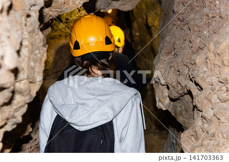 Rear view of a tourist group wearing safety helmets inside a rocky cave Rear view of a tourist group wearing safety helmets inside a rocky cave 141703363