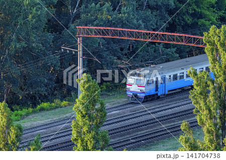 Train travels on tracks next to trees and power lines in a rural area during daylight. Train travels on tracks next to trees and power lines in a rural area during daylight. 141704738