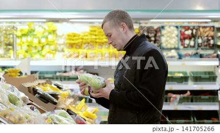 Man choosing apples at grocery store, reading labels for healthy options. Fresh produce display with vibrant colors. Everyday consumer experience in bustling supermarket aisle Man choosing apples at grocery store, reading labels for healthy options. Fresh produce display with vibrant colors. Everyday consumer experience in bustling supermarket aisle 141705266