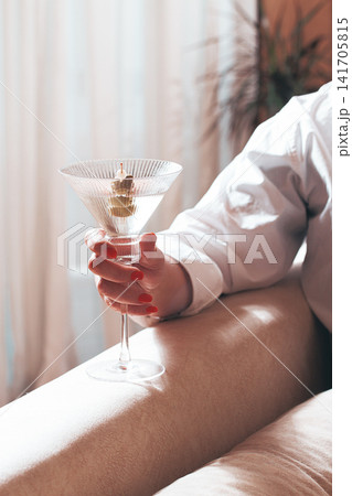 Hand holds a cocktail glass with an olive in a sunny indoor setting during the afternoon Hand holds a cocktail glass with an olive in a sunny indoor setting during the afternoon 141705815