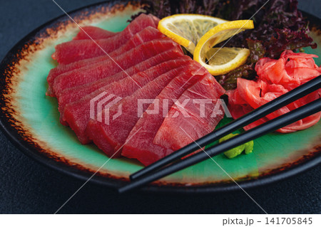 Fresh tuna sashimi served with lemon, wasabi, and pickled ginger on a dark background 141705845