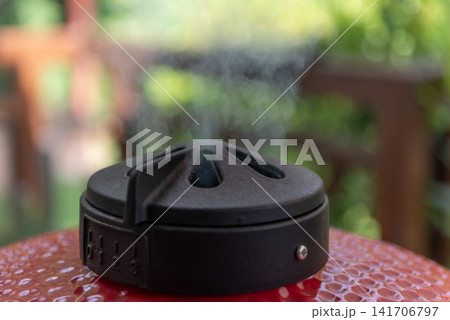 ceramic kamado grill with adjustable top vent releasing hot smoke 141706797
