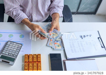 Banker, Accountant or Investor Counting Money with Gold Bars on the Table. Gold Commodity Trading and Market Analysis in Modern Office. 141707828