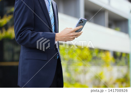 屋外でスマホを持つ20代のビジネスマン 141708926