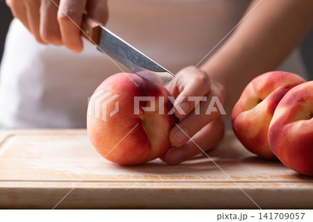 Woman hands cutting a fresh white peach with a paring knife on wooden board, homemade cooking Woman hands cutting a fresh white peach with a paring knife on wooden board, homemade cooking 141709057